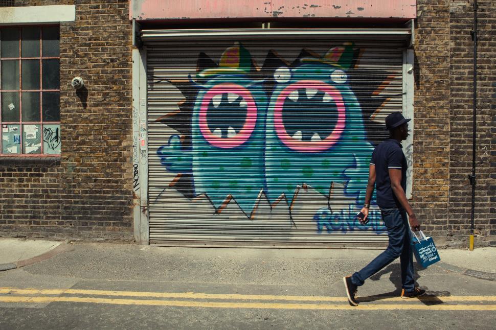 Free Image of A man walking past a graffiti wall 