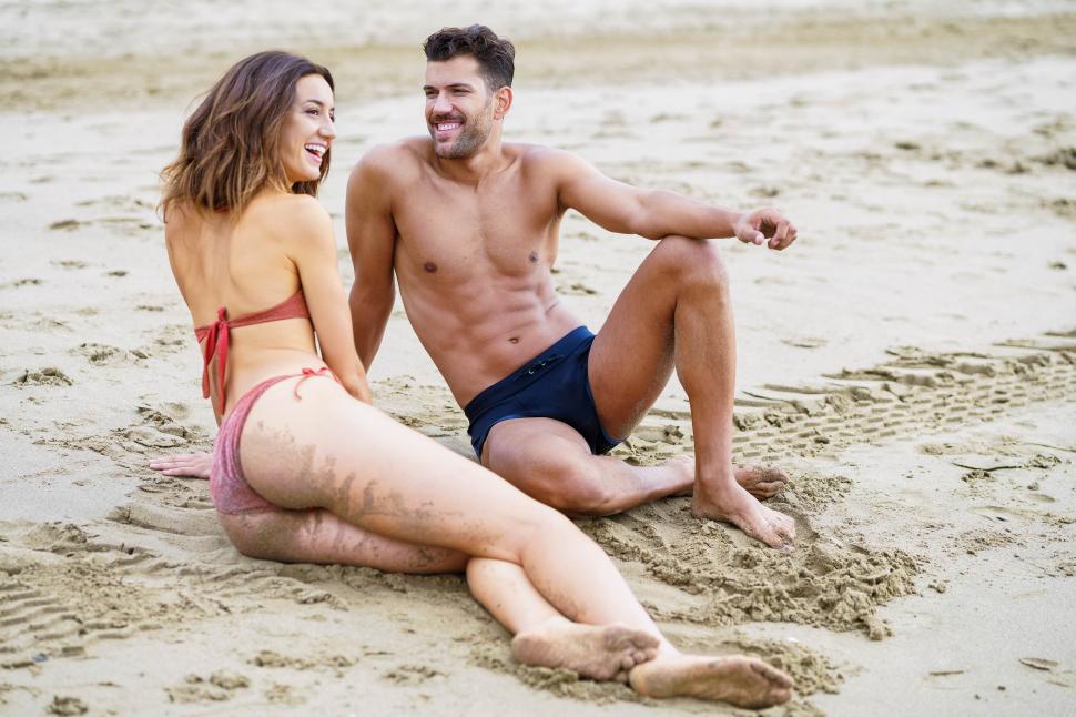 Free Image of Young couple sitting together on the sand of the beach 
