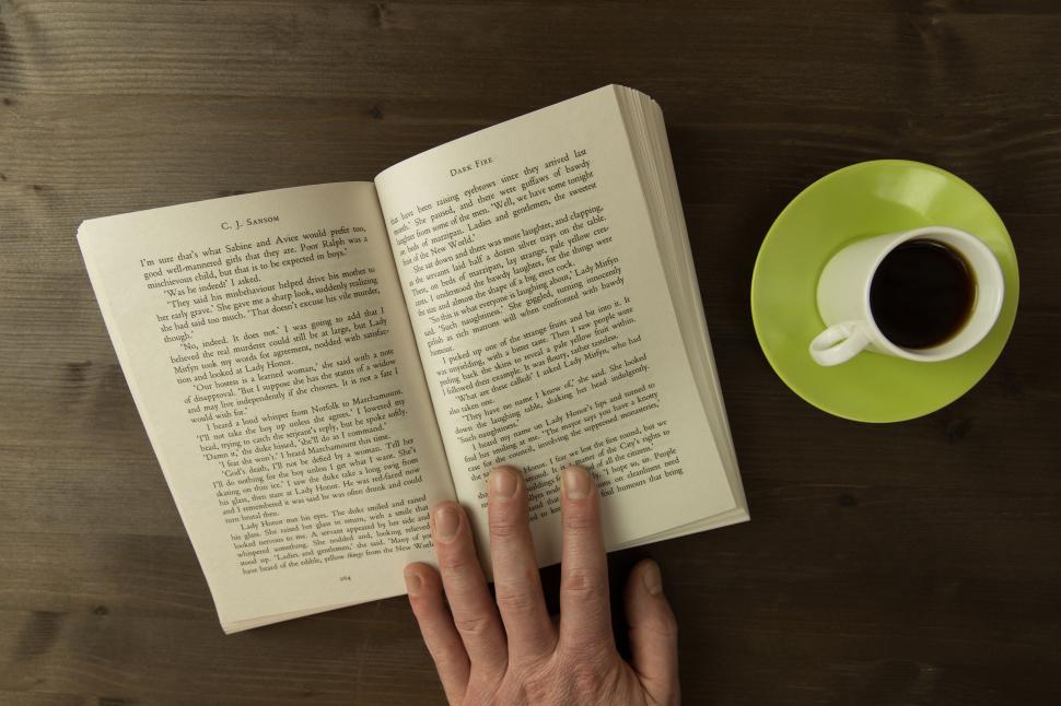 Free Image of A hand holding a book and a cup of coffee 