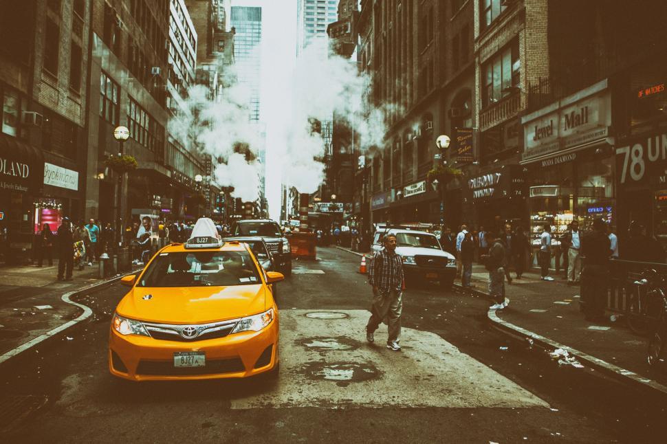 Free Image of A man walking on a street with a yellow taxi in the middle of a city 