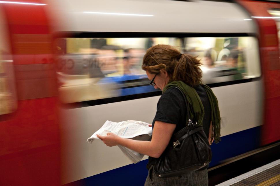 Free Image of A woman reading a newspaper near a subway car 
