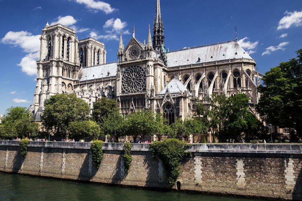 Free Image of A large building with a spire and trees by a river with notre dame de paris in the background 