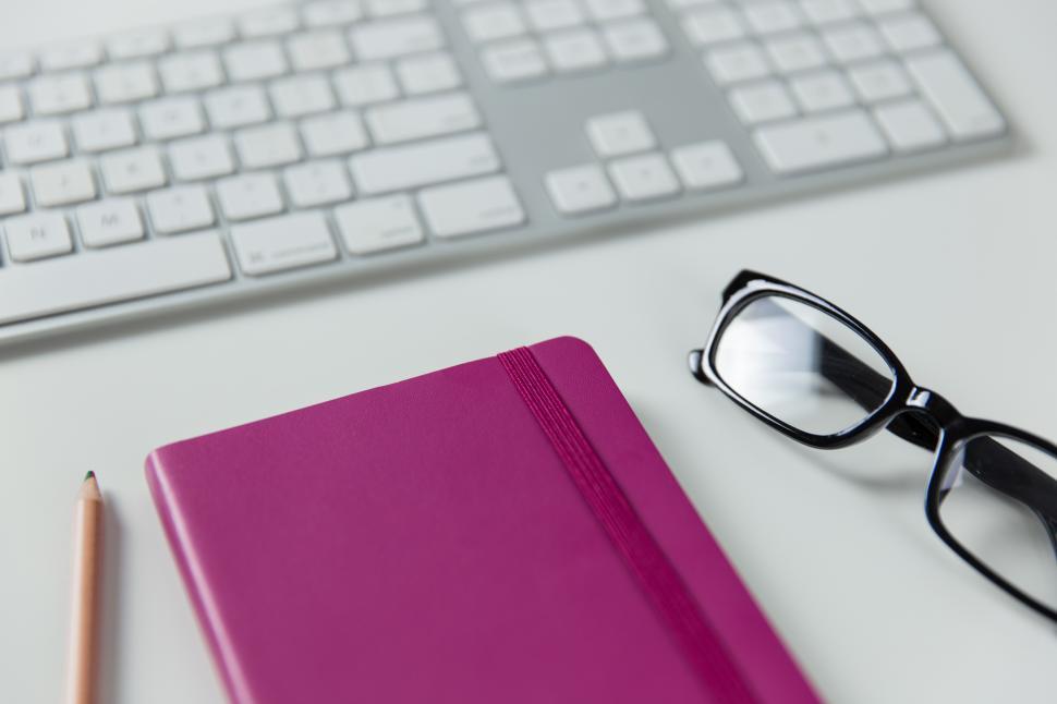Free Image of A pink notebook and glasses next to a keyboard 