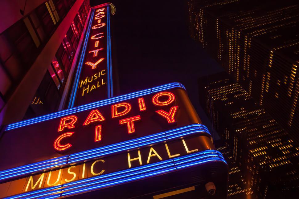 Free Image of A sign with neon lights with radio city music hall in the background 
