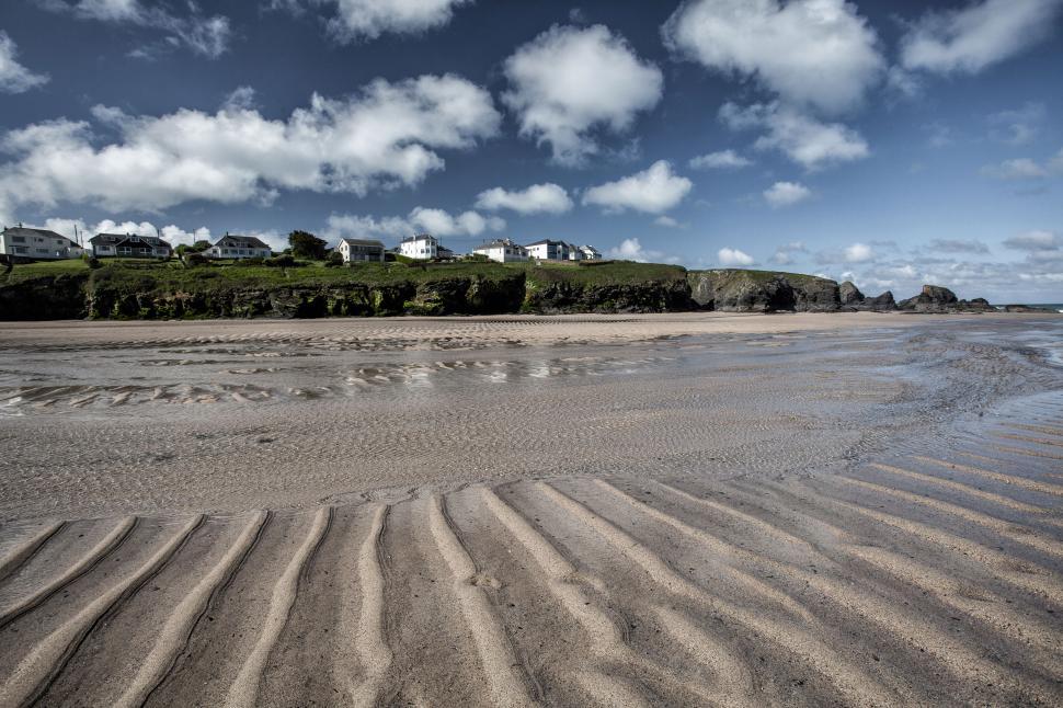 Free Image of A sandy beach with houses and a hill in the background 