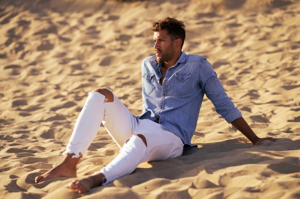Free Image of Attractive man sitting on the sand of the beach 