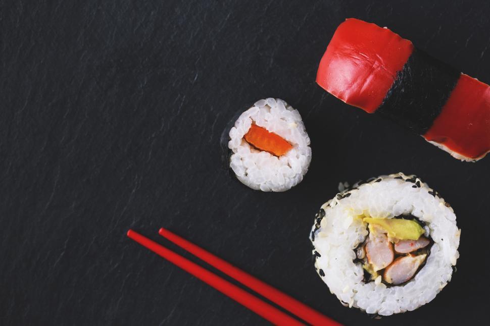 Free Image of A sushi roll and chopsticks on a black surface 