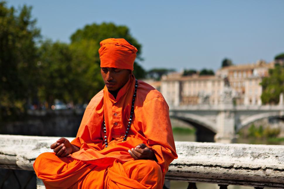 Free Image of A man in orange robe and head scarf sitting on a stone railing 