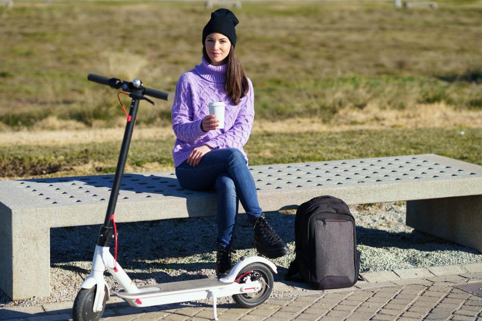 Free Image of Female student with electric scooter taking a coffee break sitting on a bench outside her college. 