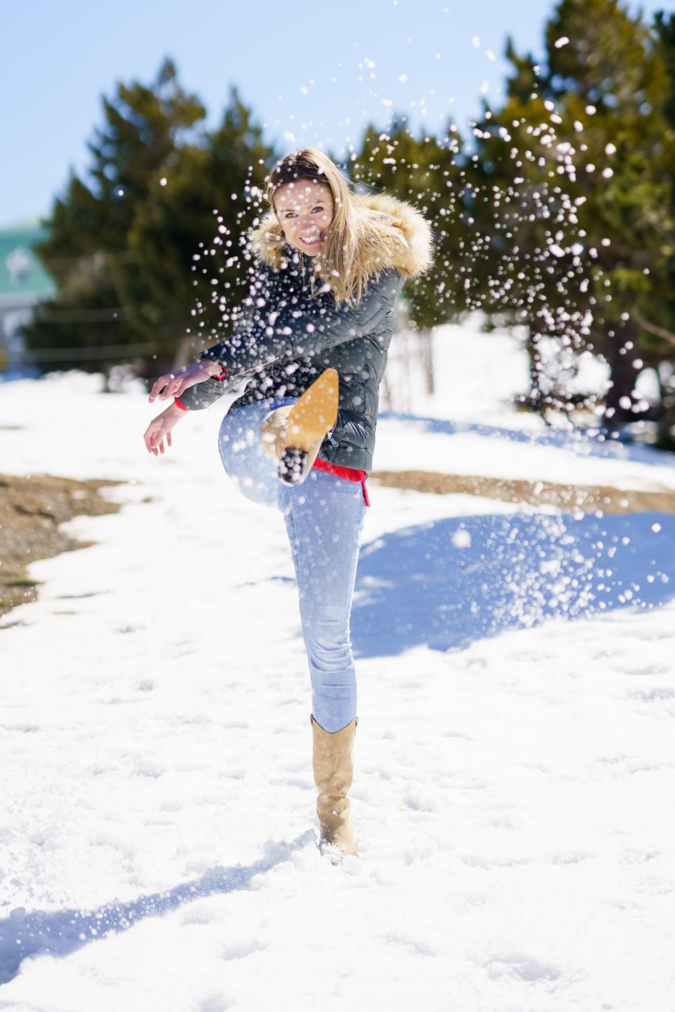 Free Image of Young happy woman kicking snow in a snow-covered forest in the mountains 