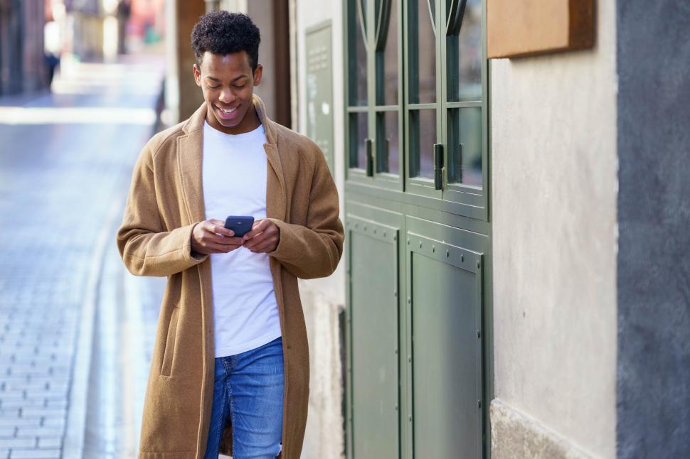Free Image of Young black man consulting his phone while walking down the street. 