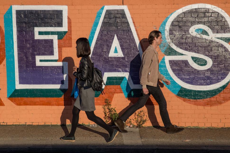 Free Image of A man and woman walking in front of a wall with graffiti 