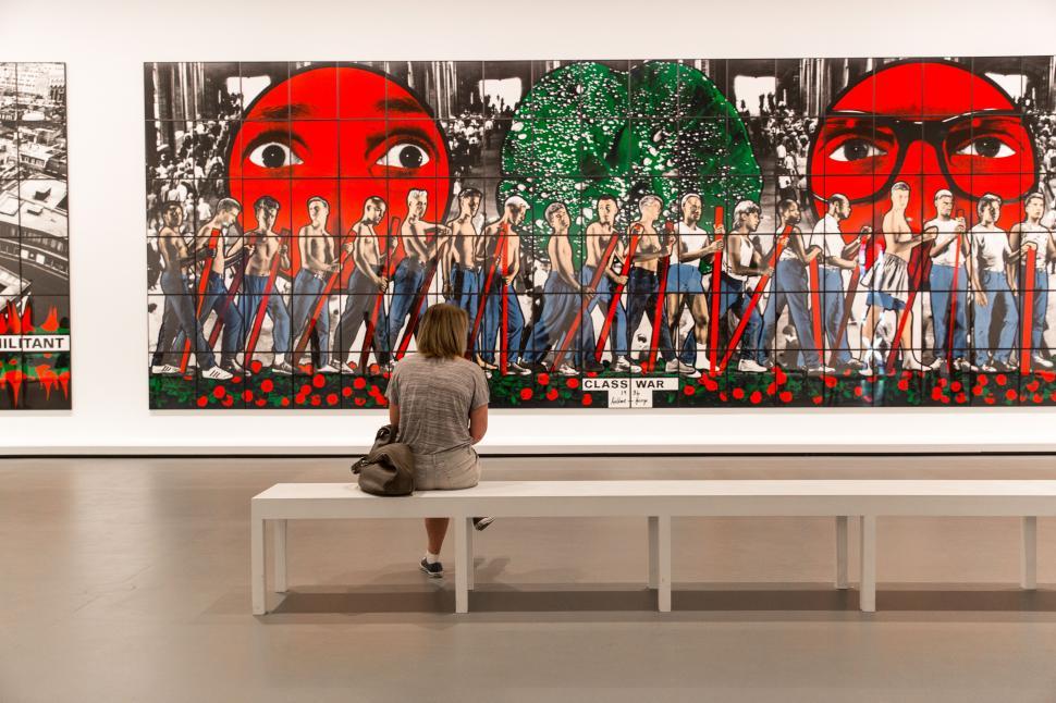 Free Image of A woman sitting on a bench looking at a large painting 