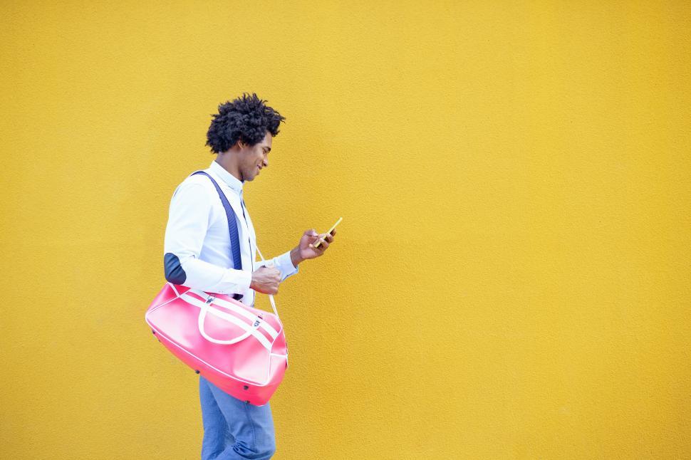 Free Image of Black man with afro hairstyle carrying a sports bag and smartphone in yellow background. 