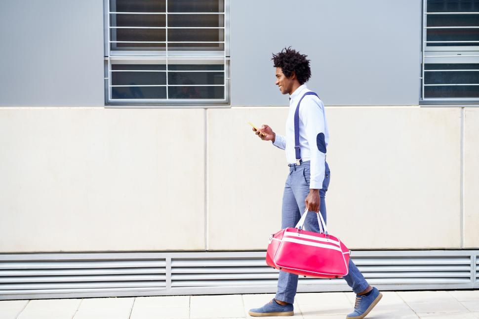 Free Image of Black man with afro hairstyle carrying a sports bag and smartphone outdoors. 