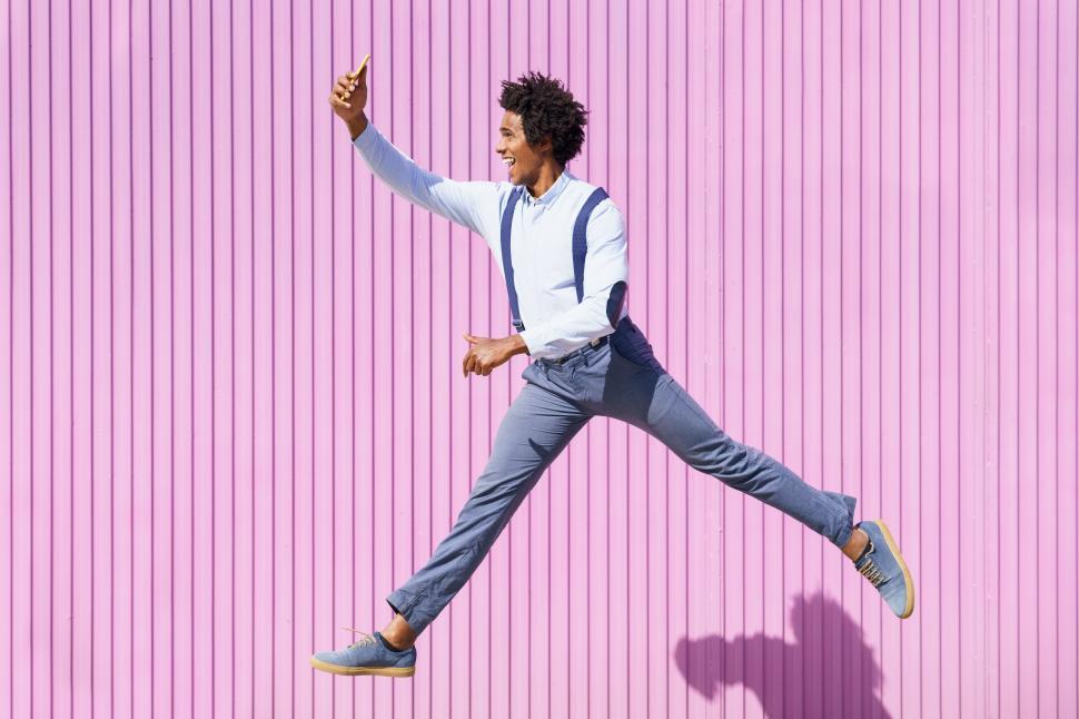 Free Image of Black man taking a selfie with his smartphone while jumping outdoors. 