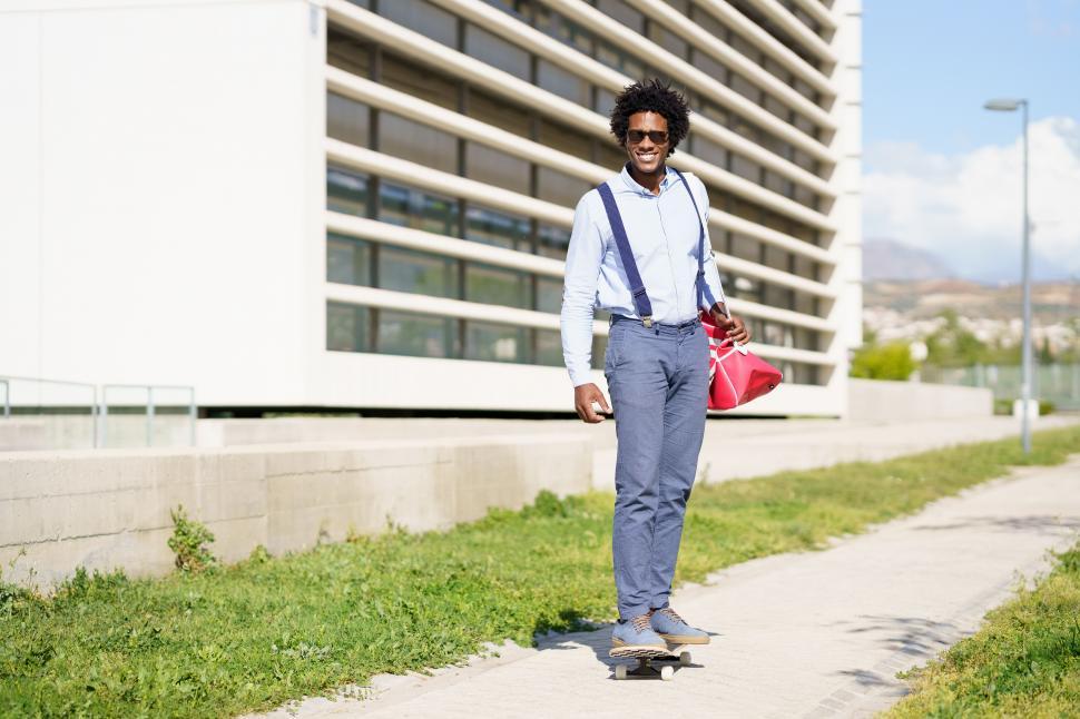 Free Image of Black businessman riding skateboard near office building. 