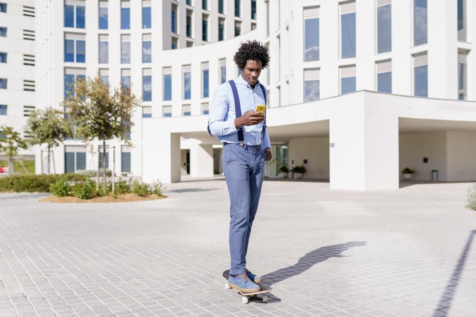 Free Image of Black businessman on a skateboard looking at his smartphone outdoors. 