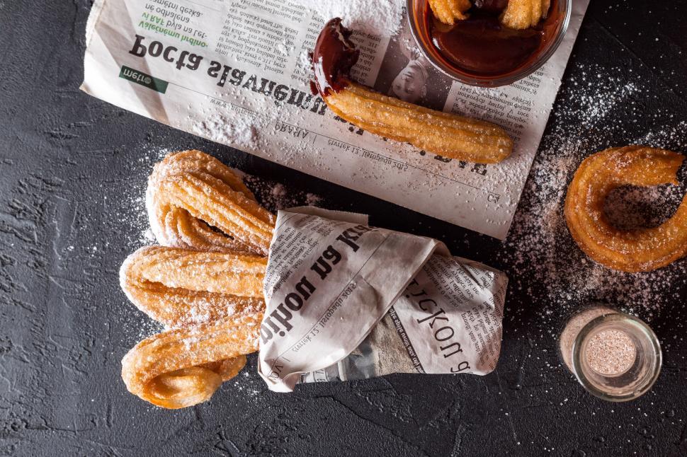 Free Image of Churros with chocolate sauce and a newspaper on a black surface 