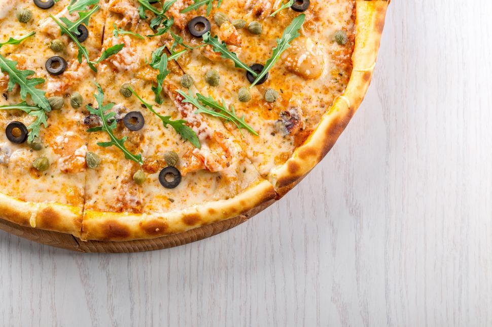 Free Image of A pizza with olives and arugula on a white surface 