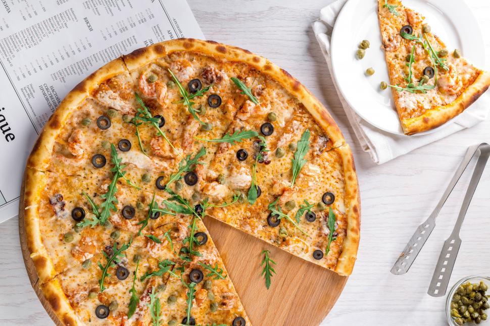 Free Image of A pizza with olives and arugula on a wooden plate 
