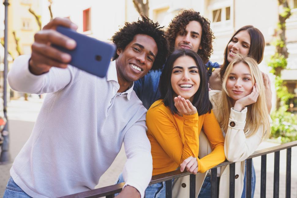 Free Image of Black man with afro hair taking a smartphone selfie with his multi-ethnic group of friends. 
