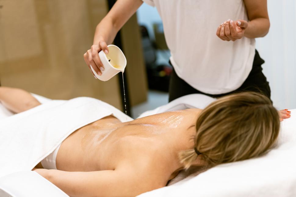 Free Image of Beauty salon professional pouring oil from a massage candle on the back of his patient. 