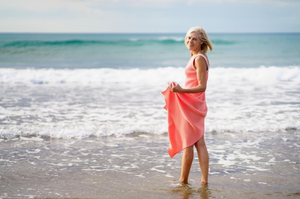 Free Image of Older woman enjoying her free time looking at the sea from the shore of the beach. 