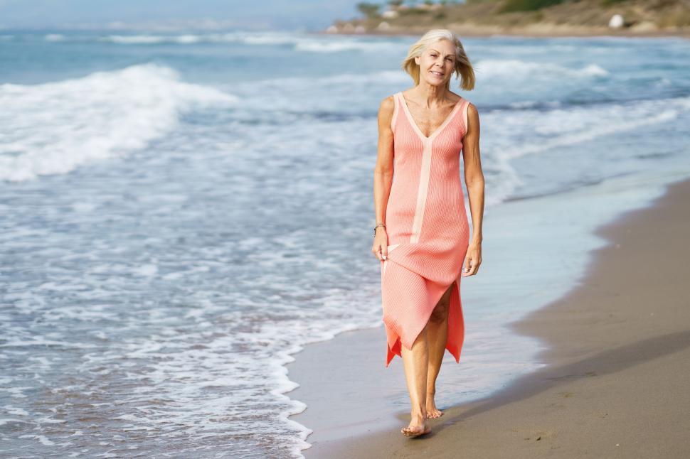 Free Image of Mature woman on shore of a beach. Elderly female enjoying her retirement at a seaside retreat. 