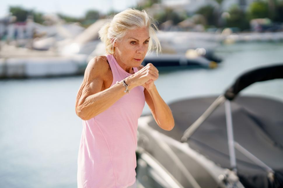 Free Image of Older woman doing shadow boxing outdoors. Senior female doing sport in a coastal port 