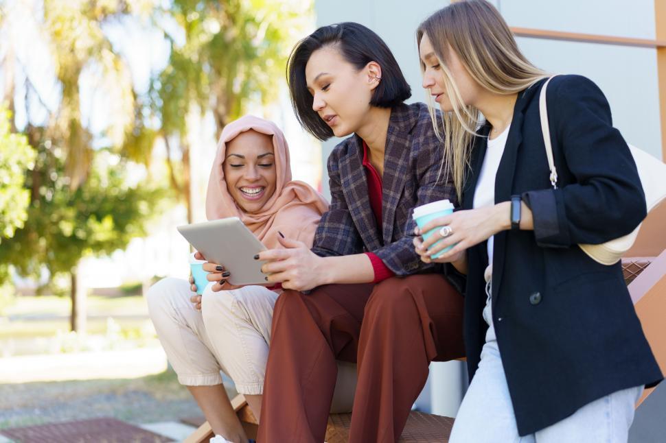 Free Image of Stylish diverse women friends sharing tablet and drinking takeaway coffee on street 