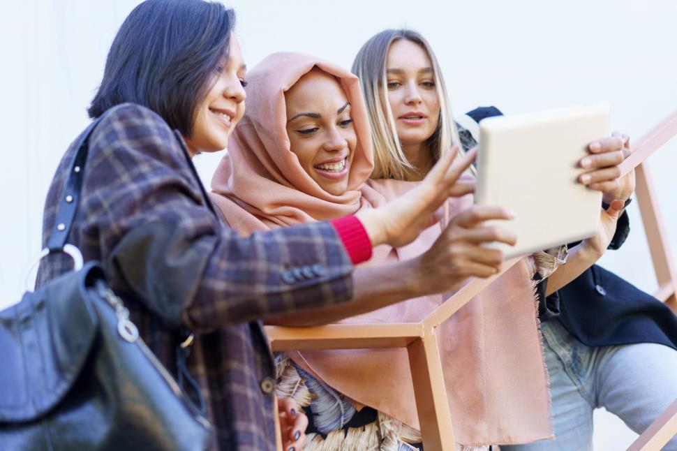 Free Image of Smiling young diverse ladies using tablet on stairs 