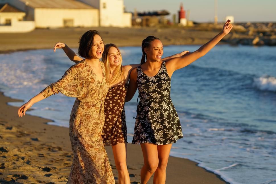 Free Image of Three funny multiethnic girls wearing summer dress laughing and having fun together on the beach. 