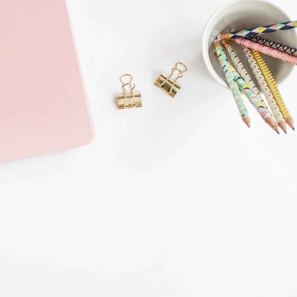 Free Image of Pencils in a cup next to a pink notebook and binder clips 