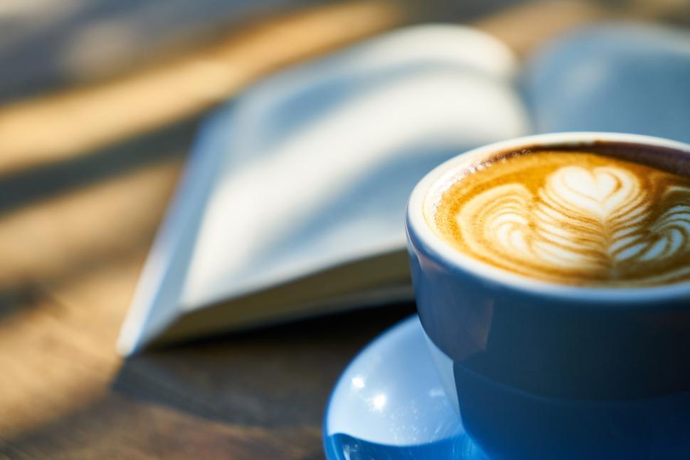 Free Image of A cup of coffee with a book and a heart shaped foam 