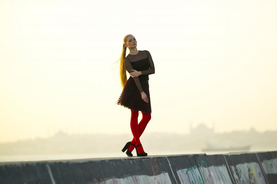Free Image of A woman in a dress and red tights standing on a concrete wall 