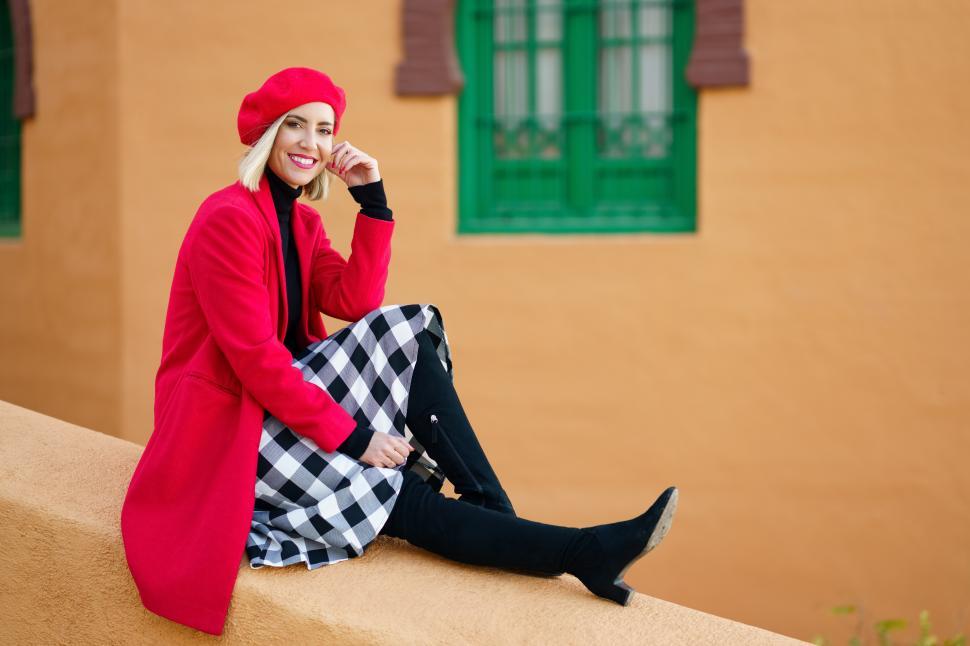 Free Image of Stylish happy woman sitting on wall near aged colored building 