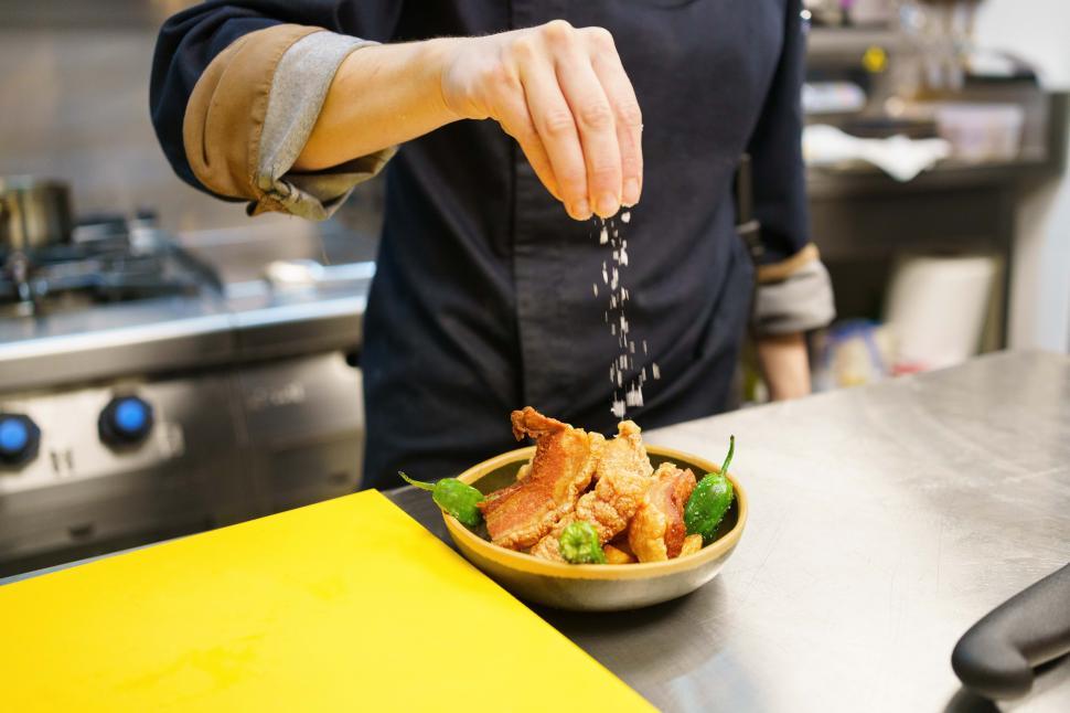 Free Image of Crop chef garnishing a dish of pork and hot peppers in restaurant 