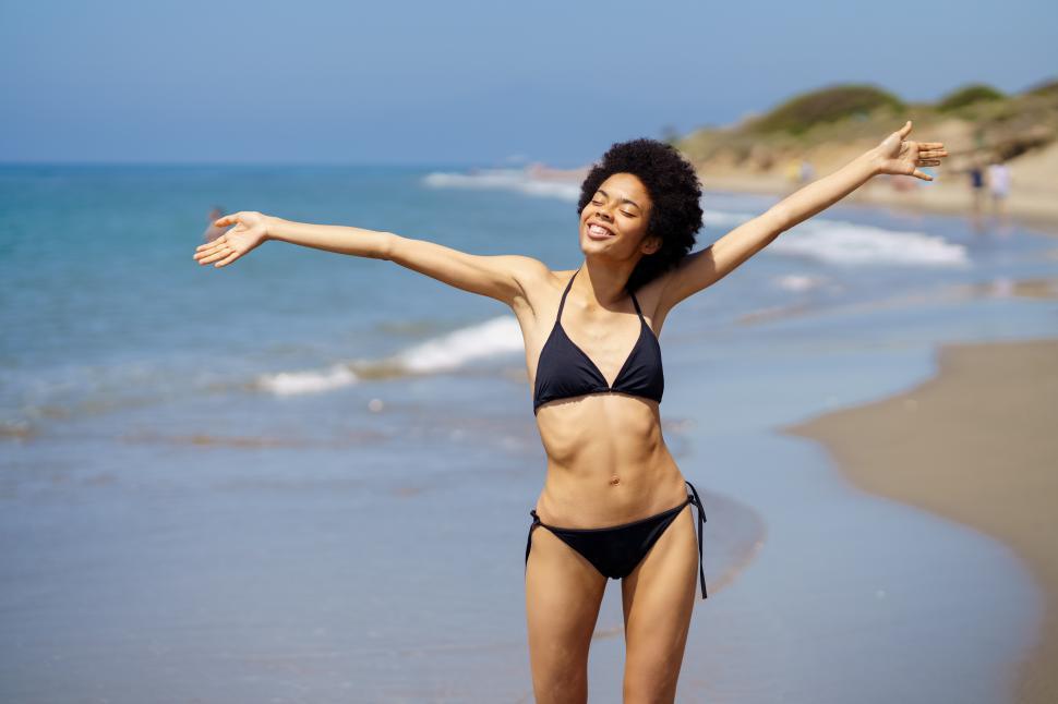 Free Image of Positive African American female opening her arms on the beach to enjoy her holiday in the sun. 