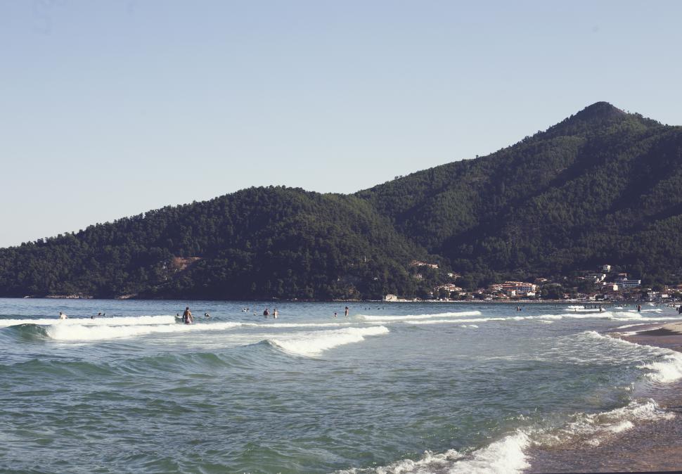 Free Image of A beach with people on water and mountains in the background 