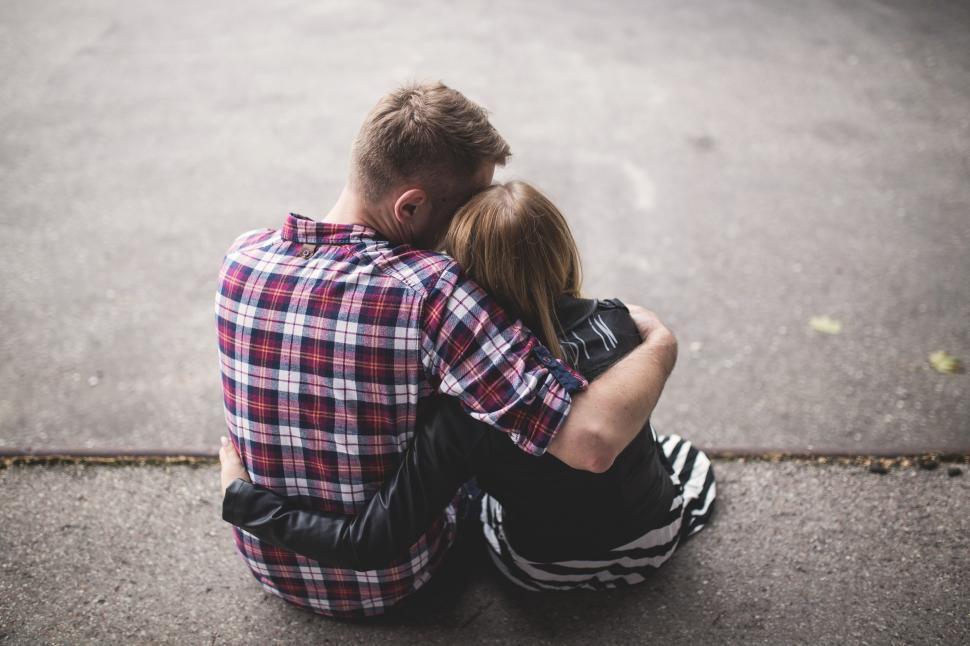 Free Image of A man and woman sitting on the ground hugging 