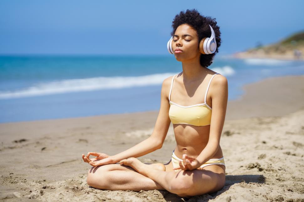 Free Image of Black girl in lotus pose doing mindfulness listening to a meditation with wireless headphones. 