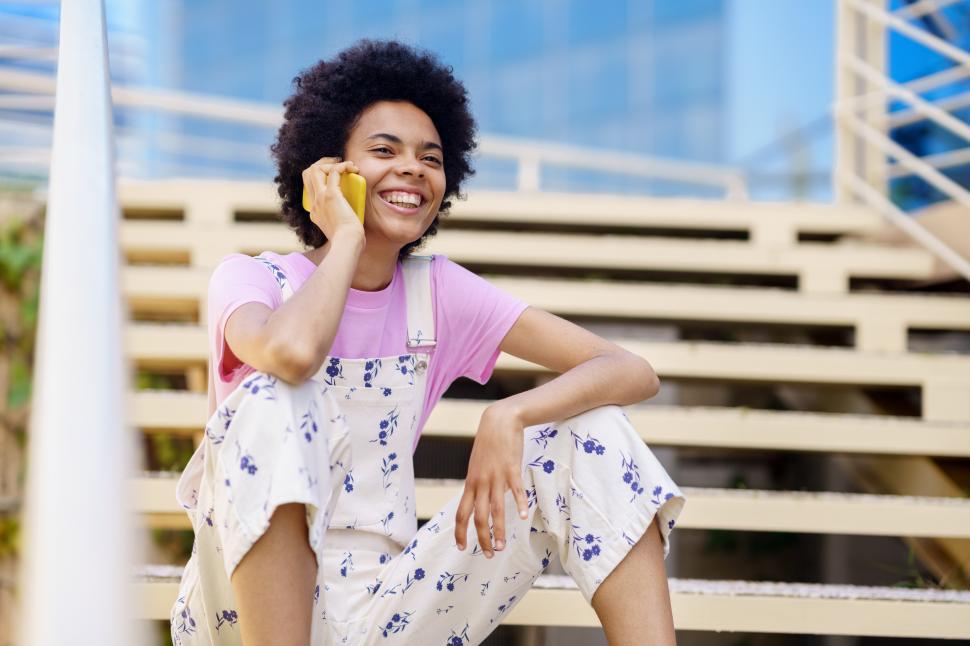 Free Image of Smiling black woman talking on her smartphone in casual clothes. 
