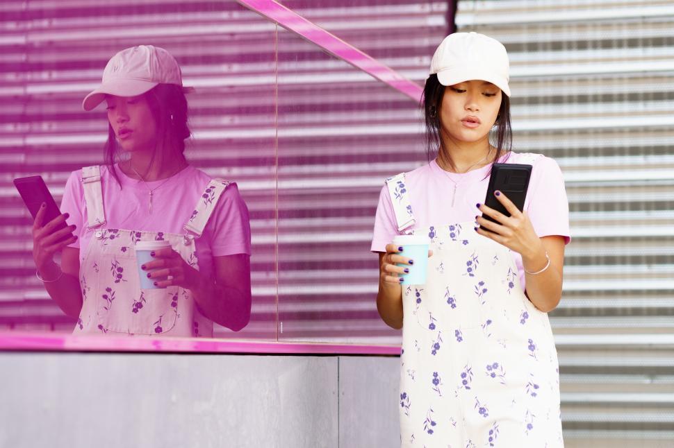 Free Image of Young Asian female using smartphone near reflective wall 