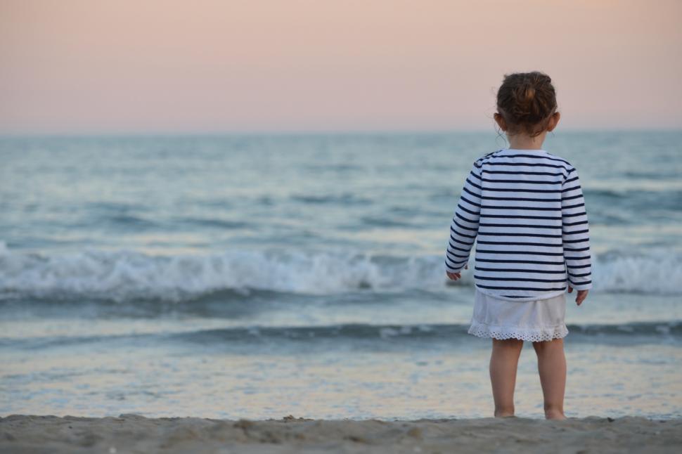 Free Image of A child standing on a beach looking at the ocean 