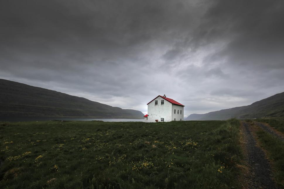 Free Image of A house in a field with water and mountains in the background 