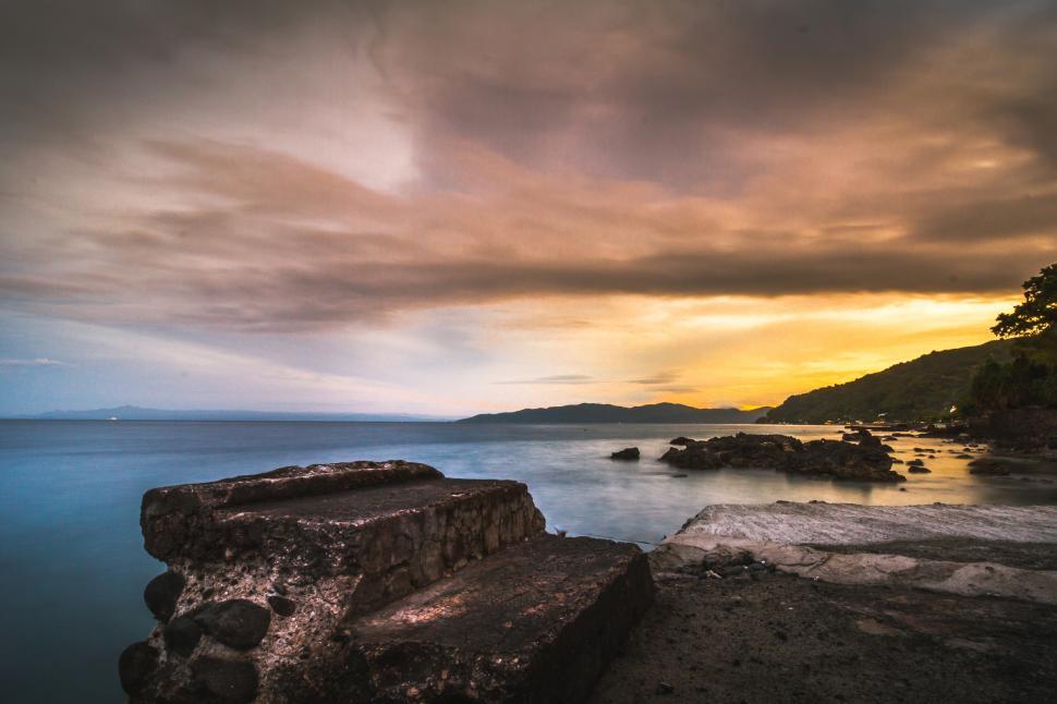 Free Image of A rocky beach with a body of water and a sunset 