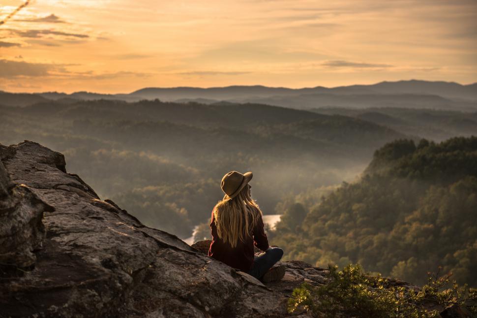 Free Image of A woman sitting on a rock looking at a valley 