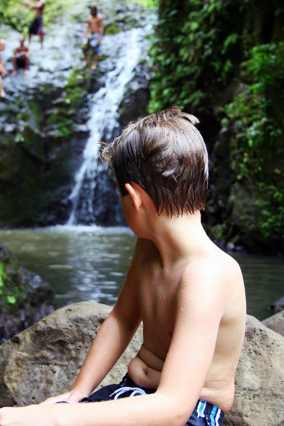 Free Image of A boy sitting on rocks near a waterfall 