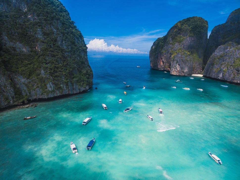 Free Image of Boats in the water with large rocks with phi phi islands in the background 